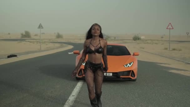 セクシーな服を着た若い女性は 砂漠の道路上の高価なスポーツカーをリードしています スローモーション — ストック動画