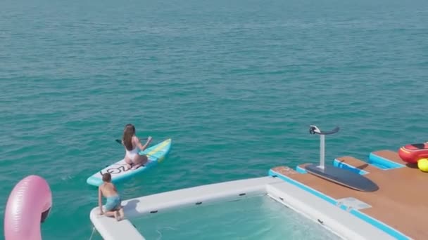 アラブ首長国連邦 ドバイ ドローンは ヨットの横にある海のSupボードに浮かんでいる白い水着の若い女性の上に飛ぶ エアリアルビュー スローモーション — ストック動画