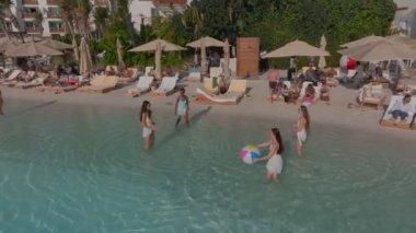 Dubai, BAE - 114 2023: bir İHA tatilci insanlarla kumlu bir sahilde uçuyor. Mayolu genç kızlar suda renkli bir topla oynuyorlar. Hava görünümü