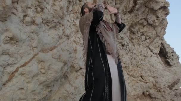 Człowiek Ubrany Jak Szaman Stojący Skale Środku Pustynnych Piasków Grający — Wideo stockowe