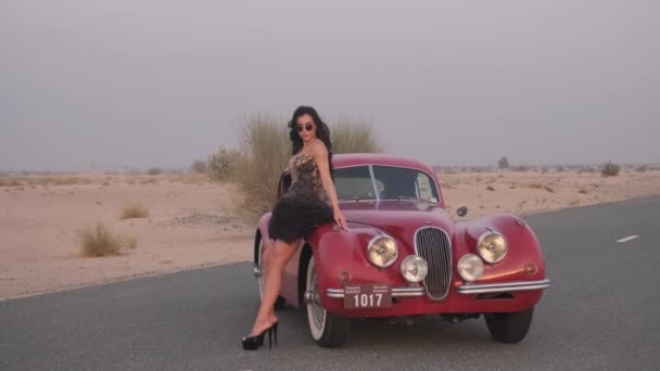 드레스와 신발에 화려한 여자는 사막의 중간에 빨간색 빈티지 자동차 도로에 — 비디오