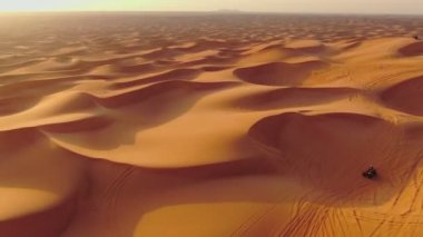 Bir dron, Birleşik Arap Emirlikleri 'nde çölün kum tepelerinden geçen dört tekerlekli bisikletlerin üzerinden uçuyor. Hava görünümü