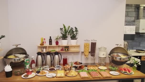 小さなホテルの朝食ルーム ソーセージ サラダ チーズ ドリンク付きのテーブルを提供しています スイカ バナナとテーブル スローモーション — ストック動画