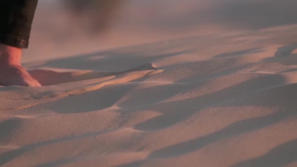 一位年轻的摄影师 手里拿着相机 赤着脚 在落日的余晖中走在沙漠的沙滩上 慢动作 — 图库视频影像