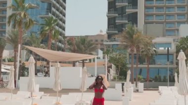 Kırmızı bikinili esmer bir kadın ve özel bir havuzda çıplak ayakla yürüyen açık renk bir elbise. Yavaş çekim.