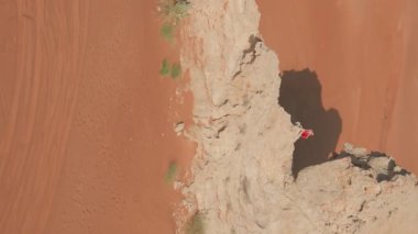 Bir dron, çölün ortasında bir uçurumun kenarında duran kırmızı elbiseli genç bir kadının etrafında uçuyor. Hava görünümü