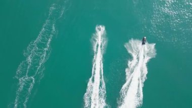 Dubai, BAE - 320 2023: Bir İHA arka planda Dubai yatı olan bir yatın yanında, denizde jet ski kullanan insanların üzerinde uçuyor. Hava görüntüsü, yavaş çekim