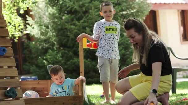 一个小男孩和他的母亲和哥哥在草坪上的一个木制鸟笼里玩彩蛋 阳光灿烂的一天 慢动作 靠近点 — 图库视频影像