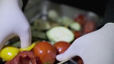 Beyaz eldivenli bir aşçı elleriyle bir konteynırda kesilmiş sebzeleri karıştırır. Yavaş Hareket, Kapat.