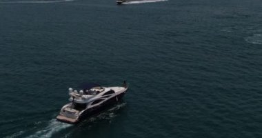 Bir İHA, sakin bir denizde şehre doğru giden özel bir teknenin yanından geçiyor. Hava görüntüsü, Ağır çekim. Dubai