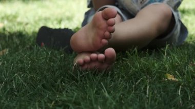 Güneşli bir günde parkta çimlerin üzerinde çıplak ayakla oturan bir gencin bacakları. Yavaş çekim, Yakın çekim.