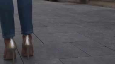 Kot pantolonlu ve açık renk bluzlu genç bir kadın yüksek topuklu ayakkabılarla sokakta yürüyor. Yavaş Hareket