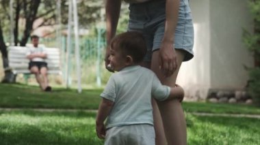 Güneşli bir günde anne ve babasıyla bahçedeki çimlerin üzerinde yürüyen küçük bir çocuk. Yavaş Hareket.