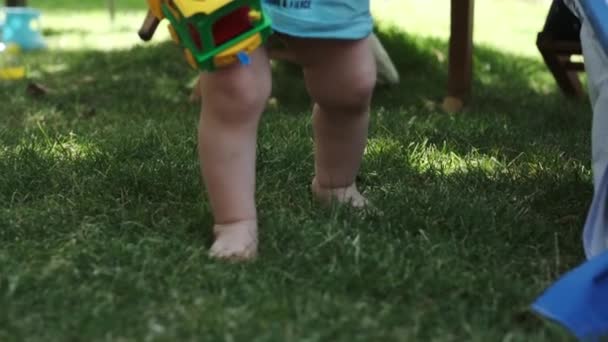 一个穿着T恤衫 没有裤子的小男孩赤脚在操场上的草地上走着 慢动作 阳光灿烂 — 图库视频影像