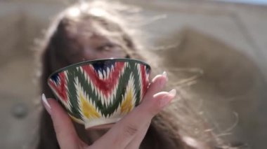 Uzun saçlı, elinde Özbek süsüsüyle boyalı bir çay fincanı tutan genç bir kadın. Yaklaş, yavaş kavram