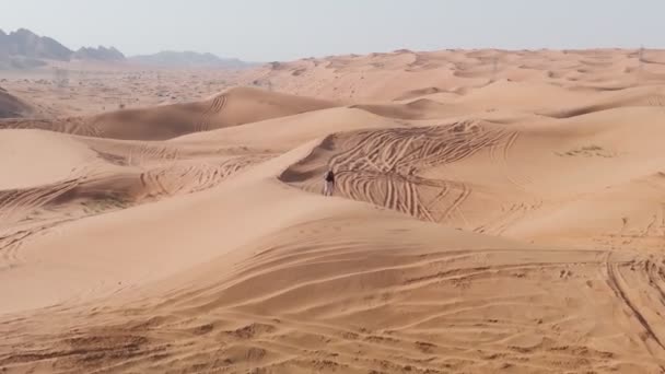 シャーマンの服を着た男が砂漠の砂の上を歩いている ドローン航空 — ストック動画