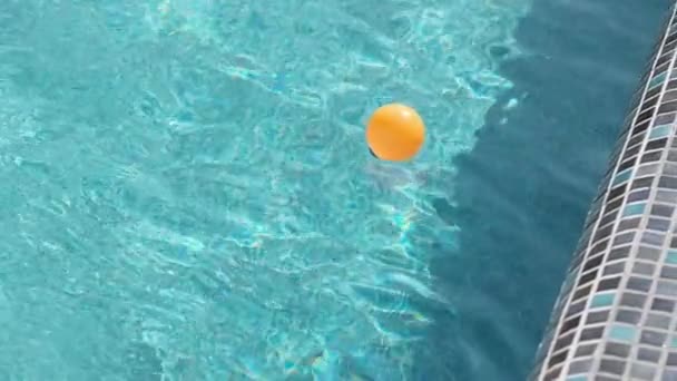 一个橙色的球漂浮在一个室外私人游泳池的波浪上 一个阳光灿烂的夏日 慢动作 — 图库视频影像