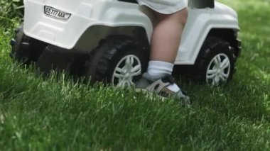 Şortlu genç bir anne, küçük oğlunu oyuncak bir arabaya bindiriyor. Park, güneşli bir gün. Yavaş Hareket, Kapat.