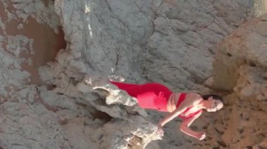 Çöldeki kumların tepesinde duran kırmızı elbiseli genç bir kadının yanından bir dron uçuyor. Hava görünümü