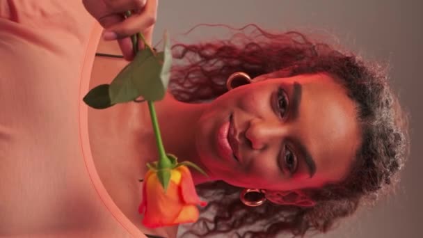 アフロヘアスタイルと明るいメイクで若い女性の肖像画 彼女は手にバラの花を持っている クローズアップ スローモーション — ストック動画