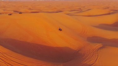 Bir dron, Birleşik Arap Emirlikleri 'nde çölün kum tepelerinden geçen dört tekerlekli bisikletlerin üzerinden uçuyor. Hava görünümü