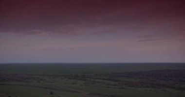 Gün batımında bulutlu bir gökyüzünün altında trafik ve çalılarla çevrili sakin bir göl. Gerçek zamanlı, 4k.