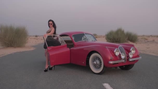 드레스와 신발에 화려한 여자는 사막의 중간에 빨간색 빈티지 자동차 도로에 — 비디오
