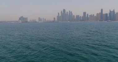 İnsansız hava aracı denizin dalgaları üzerinden kıyıdaki şehre doğru uçuyor. Dubai, Birleşik Arap Emirlikleri. Hava görünümü