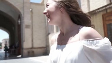 Açık beyaz elbiseli ve sandaletli, dalgalı saçlı genç bir kadın antik bir doğu şehrinde yürüyor. Yavaş Hareket, Özbekistan