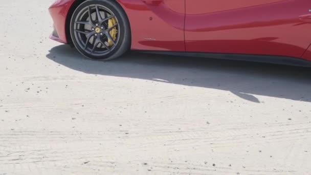 赤い高価なスポーツカーは ドバイの高層ビルを背景に堤防の砂の上に立っています スローモーション — ストック動画