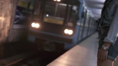 Spor kıyafetleri içinde uzun siyah saçlı genç bir kadın metro istasyonunda trenin gelişini bekliyor. Yavaş Hareket