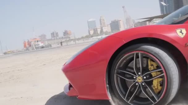 ドバイの高層ビルを背景に ビーチの砂の上に高価な赤いスポーツカーが乗っています スローモーション — ストック動画