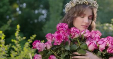 A young girl with a wreath of flowers holds a large bouquet of roses among the spring garden. Slow motion