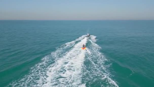 アラブ首長国連邦 ドバイ 2023 ドローンは 人々と膨脹可能なボートを引っ張るジェットスキーの上に飛ぶ エアリアルビュー スローモーション — ストック動画