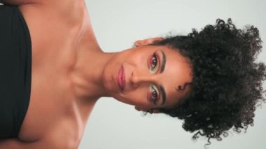 Saçları kıvırcık ve parlak makyajlı gülümseyen genç modelin dikey portresi. Yavaş Hareket, Kapat.