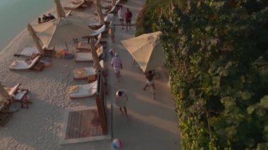 Bir İHA açık havuzun üzerinde, deniz kenarında bir sopayla uçuyor, Dubai. İnsanlar güneşleniyor, barda ve kafede dinleniyor, havuzda yüzüyor. Hava Görünümü.