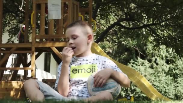 Nastolatek Szortach Koszulce Boso Siedzi Trawie Parku Piłką Pod Pachą — Wideo stockowe