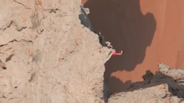 Bir dron, çölün ortasında bir uçurumun kenarında duran kırmızı elbiseli genç bir kadının etrafında uçuyor. Hava görünümü