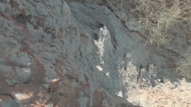 Drona, kumlu bir çölün ortasında uçurumun kenarında duran parlak kırmızı elbiseli genç bir kadının üzerinden uçuyor. Hava görünümü