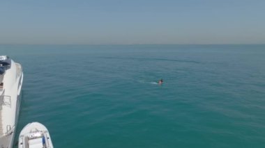 Bir insansız hava aracı, açık denizde, özel bir yatın yanında, elektrikli folyo üzerinde yelken açan bir adamın üzerinden uçuyor. Hava görüntüsü, Ağır çekim.