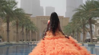 Uzun pembe elbiseli siyah saçlı esmer bir kadın fıskiyenin kenarında kameradan yürür. Slow Motion, Dubai, BAE