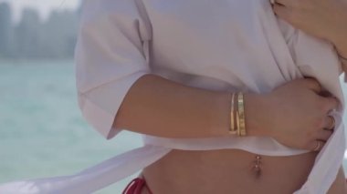 Kırmızı bikinili, kısa beyaz gömlekli, kumlu sahilde yalınayak duran genç, seksi esmer kadın. Yavaş Hareket