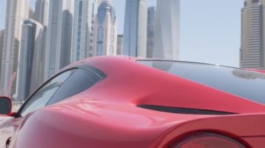Pahalı kırmızı bir spor araba Dubai 'deki gökdelenlerin arka planına karşı sahilin kumu üzerinde ilerliyor. Yavaş Hareket