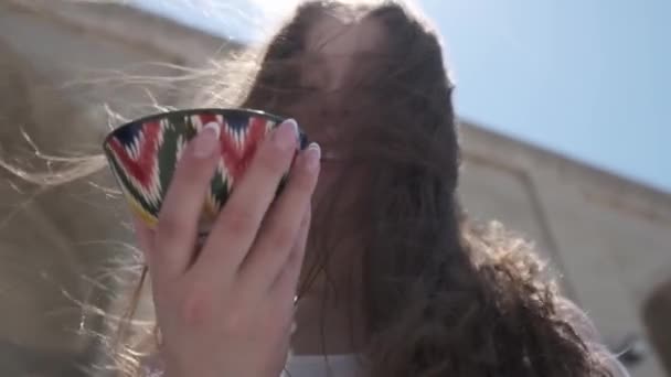 一个留着长发的年轻女子手里拿着一个漆有乌兹别克装饰品的陶瓷茶杯 慢一点 — 图库视频影像