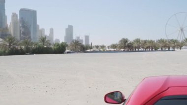 Kırmızı pahalı bir spor araba Dubais gökdelenlerinin arka planına karşı setin kumu üzerinde duruyor. Yavaş Hareket