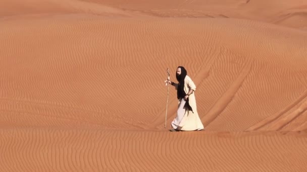 シャーマンの服を着た男が砂漠の砂の上を歩いている ドローン航空 — ストック動画