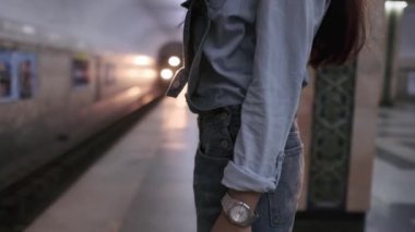 Spor kıyafetleri içinde uzun siyah saçlı genç bir kadın metro istasyonunda trenin gelişini bekliyor. Yavaş Hareket