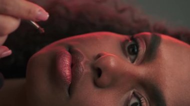 Makyöz, fotoğraf stüdyosunda genç ve çekici bir mankenin dudaklarına ruj sürüyor. Yavaş Hareket.