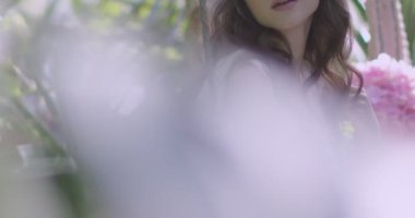 A young beautiful girl in a wreath of flowers swings on a swing among a green garden. Slow motion