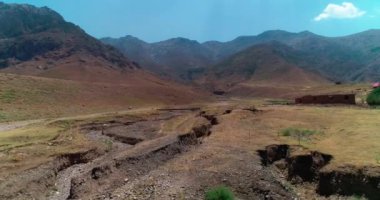 Bir dron dağların ve tepelerin arasında kurumuş bir nehrin üzerinde uçuyor. Hava görüntüsü, yavaş çekim